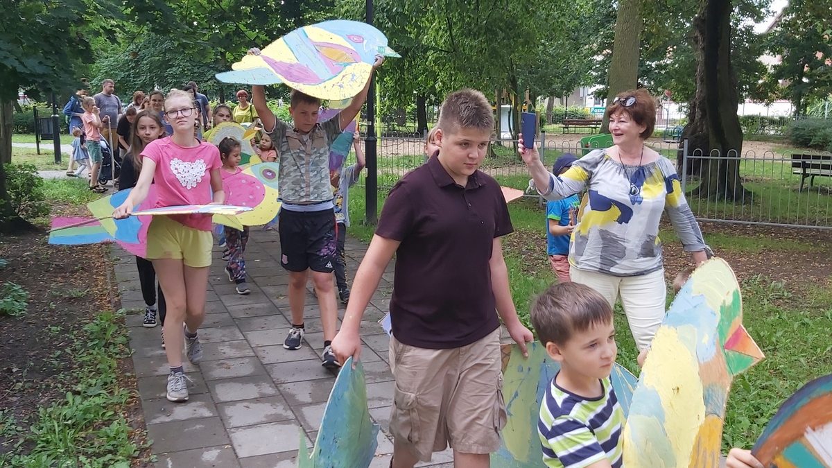 Przemarsz grupy dzieci z kolorowymi ptakami przez park