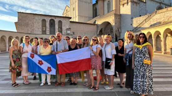Członkinie chóru z flagami Polski i Murowanej Gośliny  pozują do zdjęcia.