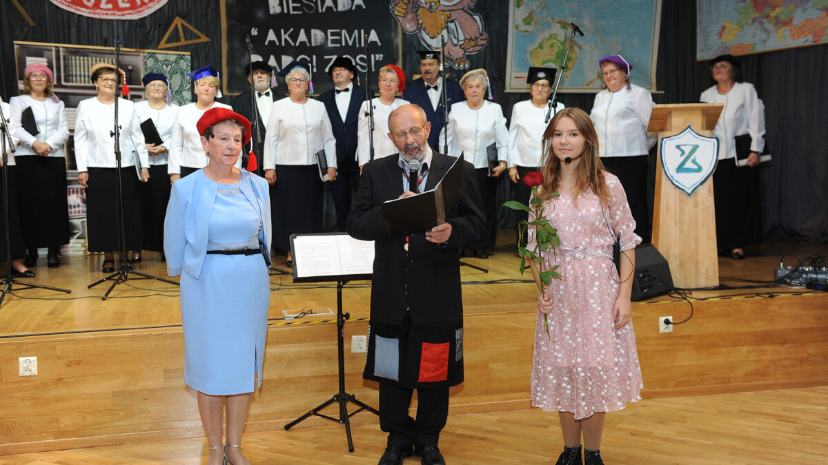 Trzech aktorów stoi przy scenie w tle zespół Goślinianka.