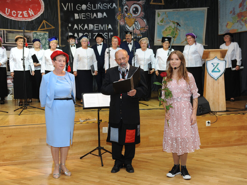 Trzech aktorów stoi przy scenie w tle zespół Goślinianka.