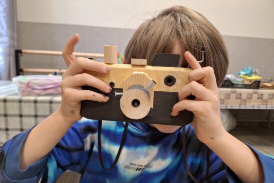 Chłopiec z drewnianym aparatem fotograficznym.
