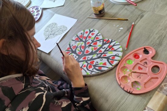 Dziewczynka maluje drzewko na płótnie w kształcie serca