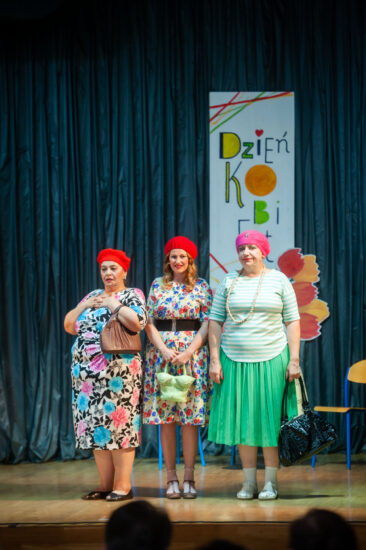 Trzy artystki kabaretowe w barwnych sukienkach i beretach moherowych na scenie
