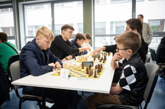 Młodsi szachiści przy stole, szachownice, zegary.