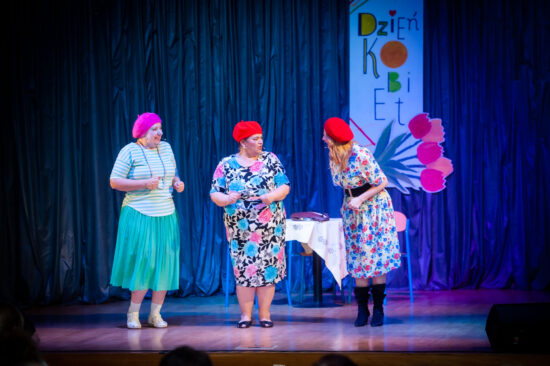 Trzy artystki kabaretowe w barwnych sukienkach i beretach moherowych na scenie